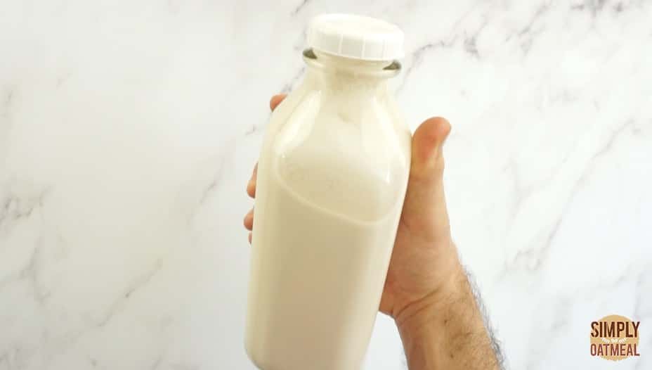 hand holding almond milk being stored in a glass milk bottle
