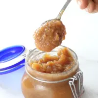 A spoon scooping apple butter out of a glass jar