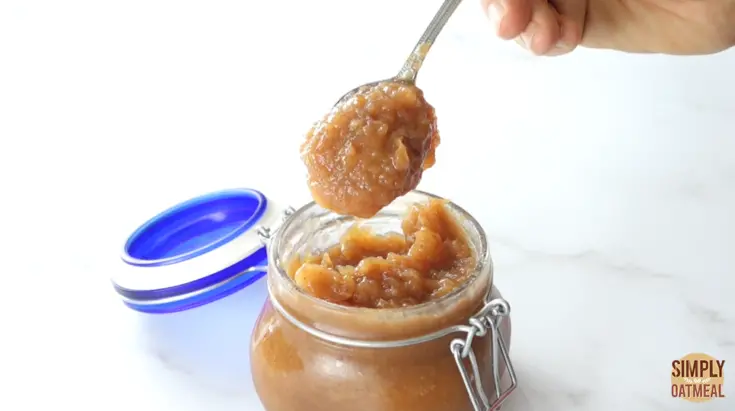 A spoon scooping apple butter out of a glass jar