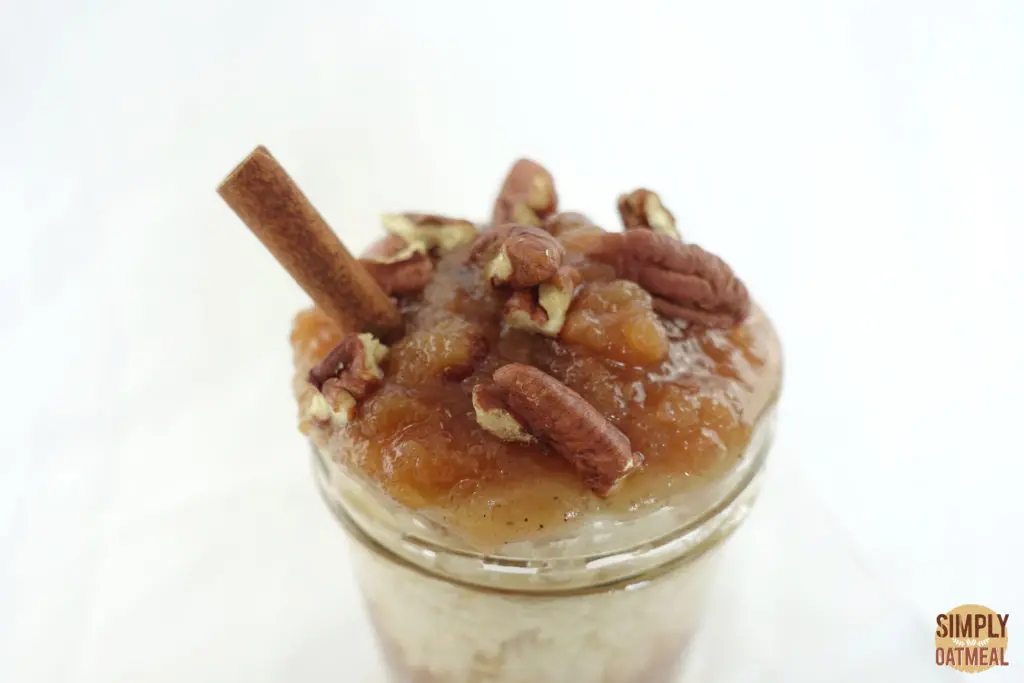 Apple Cider Overnight Oats 2 Apple cider overnight oats topped with applesauce, chopped pecans and a cinnamon stick in a glass bowl.