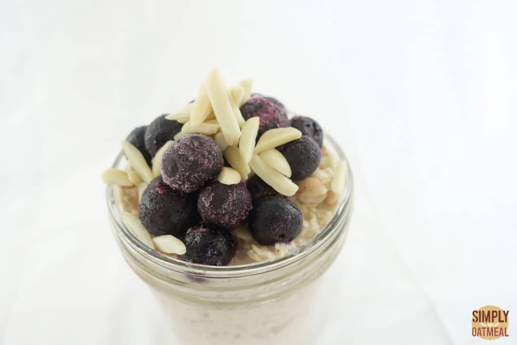Apple juice overnight oats topped with blueberries and slivered almonds served in a glass bowl.