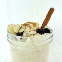 A single serving of apple pie overnight oats in a mason jar. The soaked oats are topped with whipped cream, fresh blueberries, slivered almonds and a sprinkle of cinnamon.