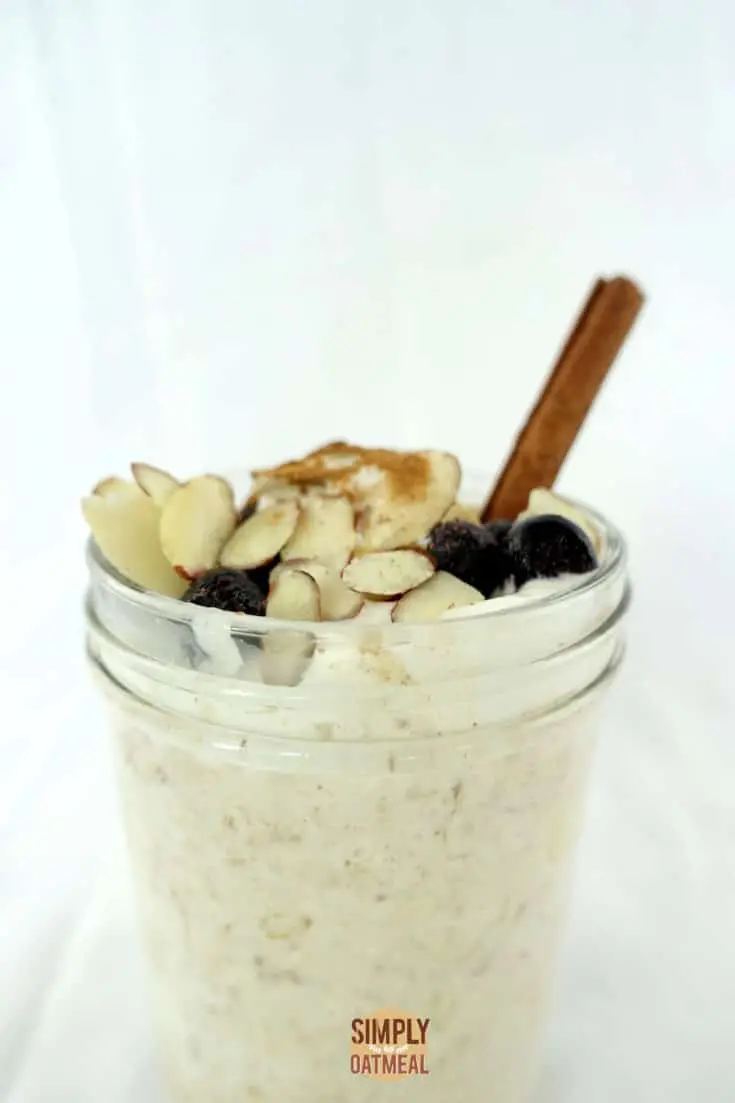 A single serving of apple pie overnight oats in a mason jar. The soaked oats are topped with whipped cream, fresh blueberries, slivered almonds and a sprinkle of cinnamon.