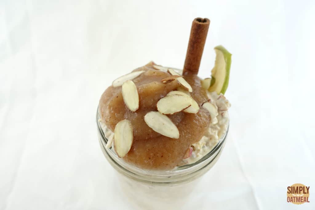 The applesauce overnight oats are topped with applesauce, sliced almonds and dried apple chip. Cinnamon stick is used as a garnish.