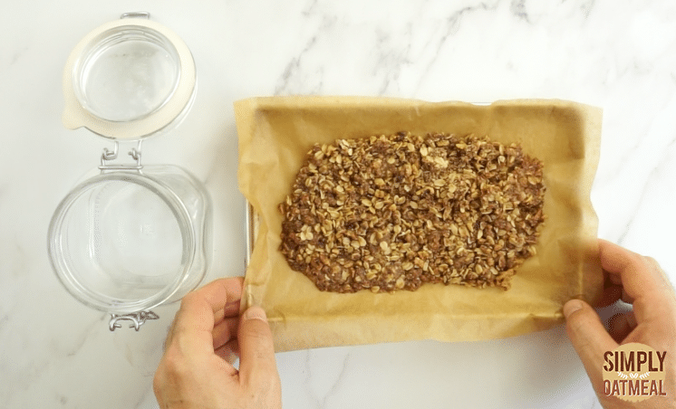 Baked oatmeal crumble topping on a baking sheet fresh out of the oven. An airtight glass jar is prepared to store the baked oatmeal crumble topping.