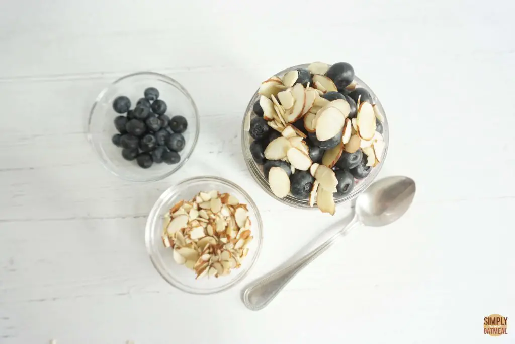 Sliced almonds, fresh blueberries and overnight oatmeal in a glass bowl.