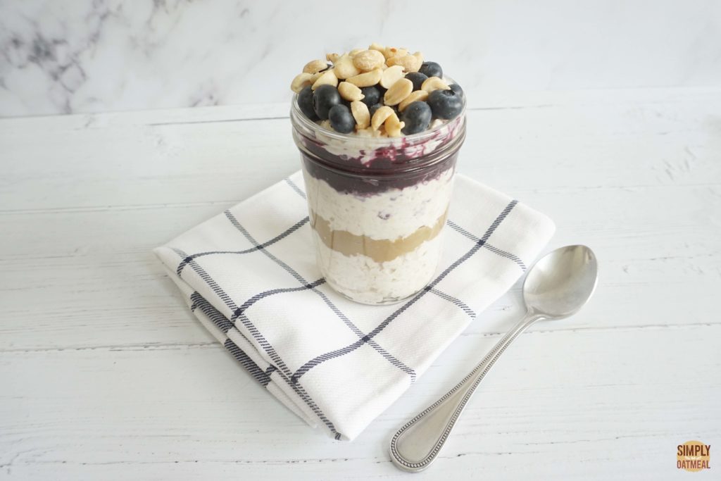 Overnight oats layered with peanut butter and blueberry jam inside a glass container.