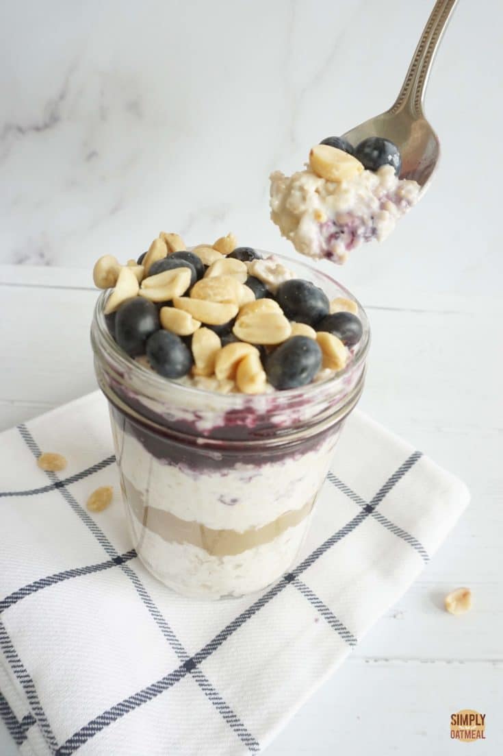 Glass bowl filled with blueberry peanut butter overnight oats. A spoon is taking a large scoop.