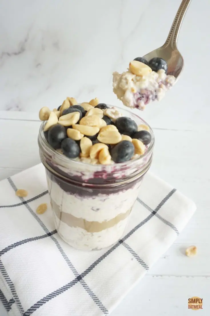 Glass bowl filled with blueberry peanut butter overnight oats. A spoon is taking a large scoop.