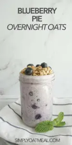 blueberry pie overnight oats in a glass jar topped with crispy pie topping and fresh blueberries.
