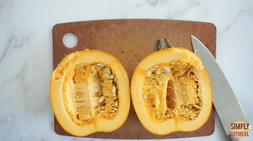 Cut pumpkin in half with large knife Pumpkin cut in half on cutting board with a large knife.