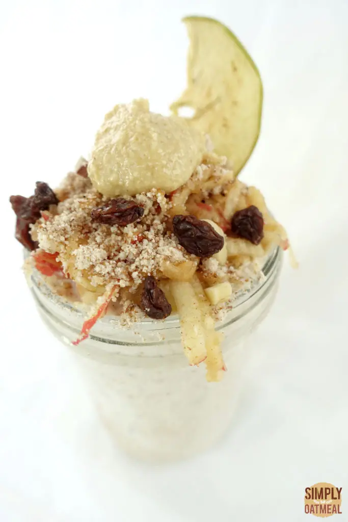 One serving of grated apple overnight oats topped with raisons, peanut butter and an apple chip.