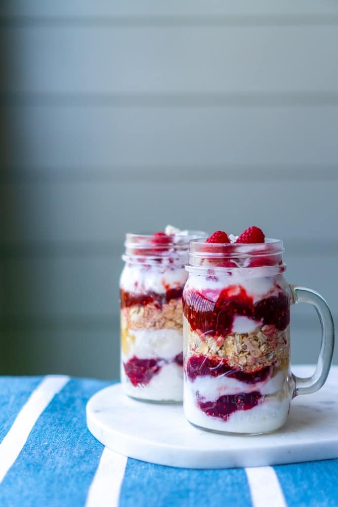Overnight oats that have been soaked in a glass jar. The soaked oatmeal has been sandwiched in between layers of raspberry sauce and yogurt.