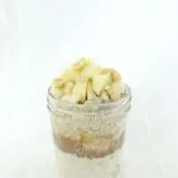 Overnight oats and peanut butter layered in a tall glass container topped with fresh chopped apple and peanuts.
