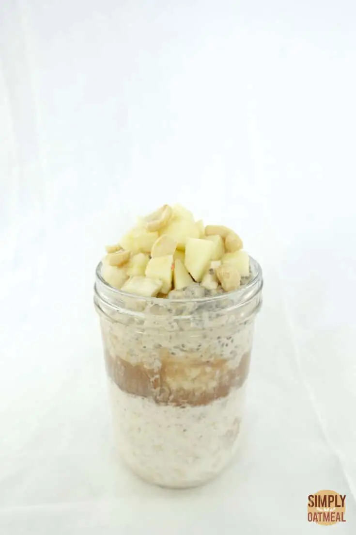 Overnight oats and peanut butter layered in a tall glass container topped with fresh chopped apple and peanuts.