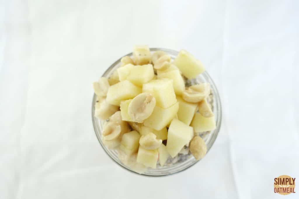 Overnight oats topped with diced apples and peanuts in a glass bowl.