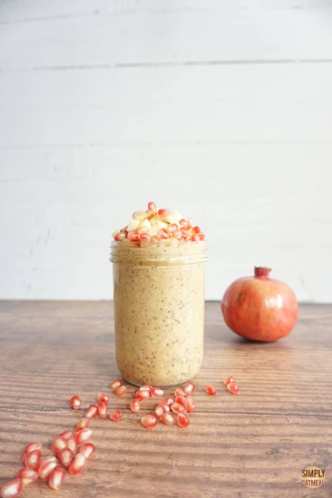 Pumpkin chia overnight oats in a tall glass container, Pomegranate seeds sprinkled across the table.
