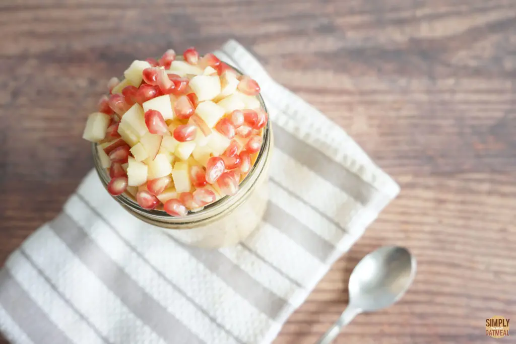 Pumpkin chia overnight oats in a glass bowl topped with chopped apple and pomegranate seeds