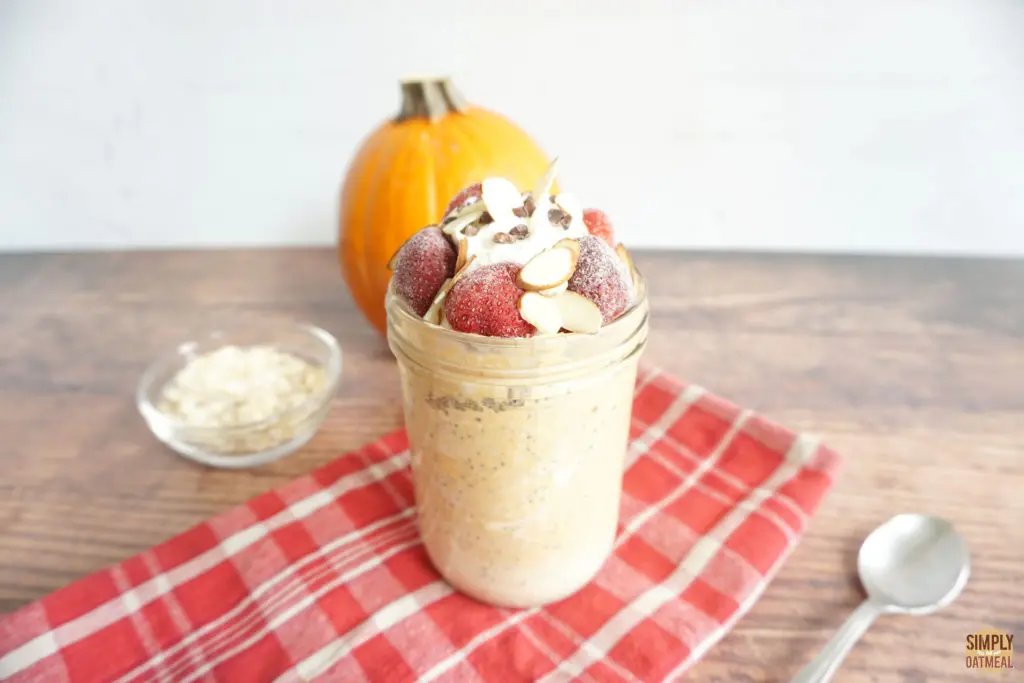 pumpkin greek yogurt overnight oats in a mason jar topped with whipped cream, strawberries and sliced almonds.