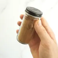 Hand holding pumpkin pie spice inside glass spice container