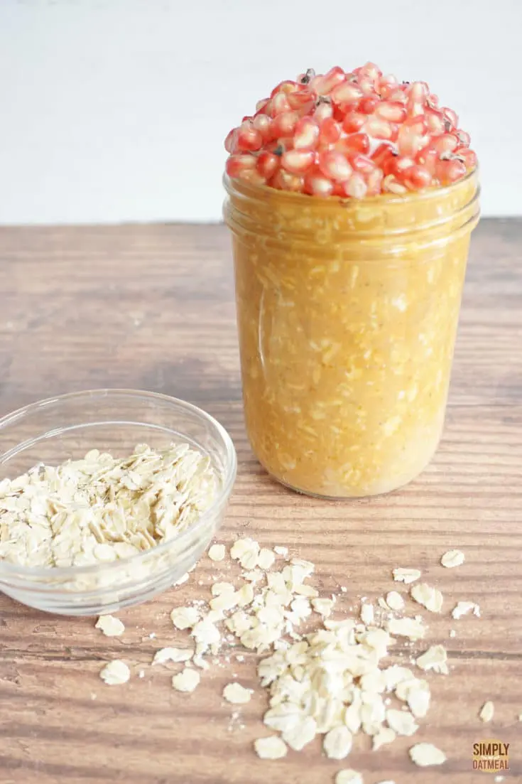 pumpkin puree overnight oats topped with pomegranate seeds. Rolled oats are sprinkled across the wood table