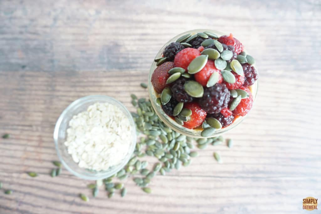 pumpkin seed overnight oats in a small glass bowl topped with mixed berries and pepita seeds