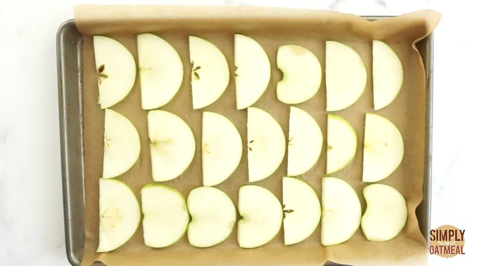 raw apple slices spread out evenly on a baking sheet.