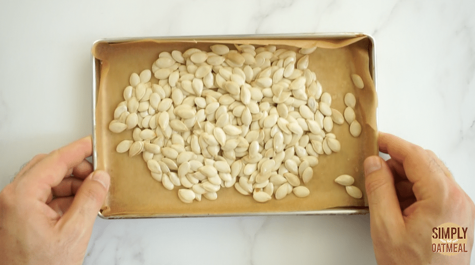 raw pumpkin seeds spread out on a sheet pan and about to go into a hot oven for about 15 minutes.