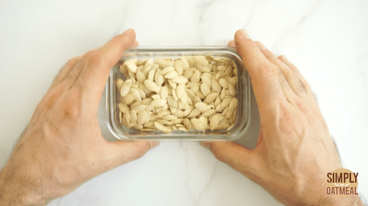 Roasted pumpkin seeds being stored in a glass container. The seeds have fully cooled and while last about 2 weeks.