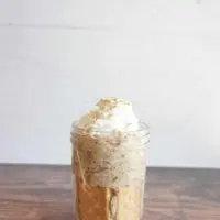 Banana bread overnight oats served in a tall glass container with whipped cream and a sprinkle of ground cinnamon