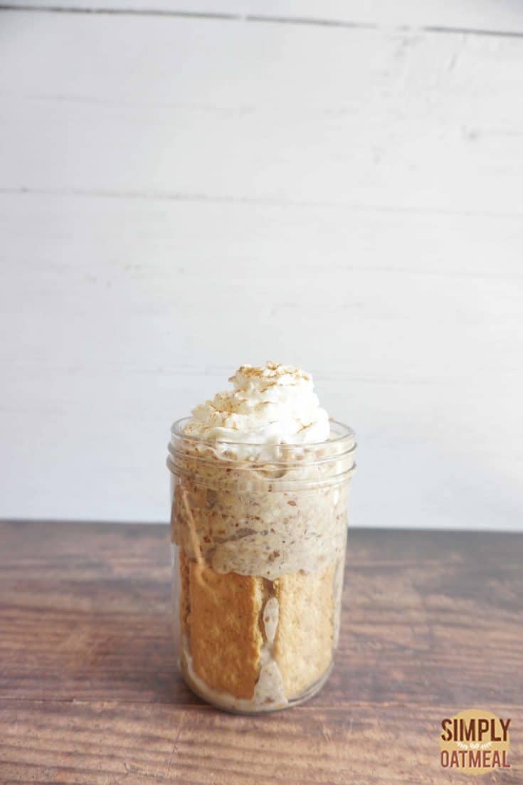 Banana bread overnight oats served in a tall glass container with whipped cream and a sprinkle of ground cinnamon