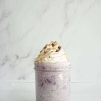 Mason jar filled with blueberry chia overnight oats and topped with whipped cream, cocoa nibs and a sprinkle of cinnamon.