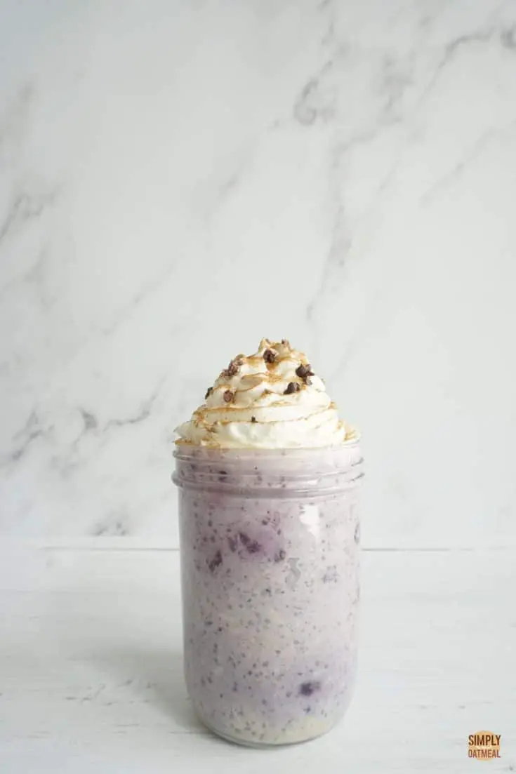 Mason jar filled with blueberry chia overnight oats and topped with whipped cream, cocoa nibs and a sprinkle of cinnamon.