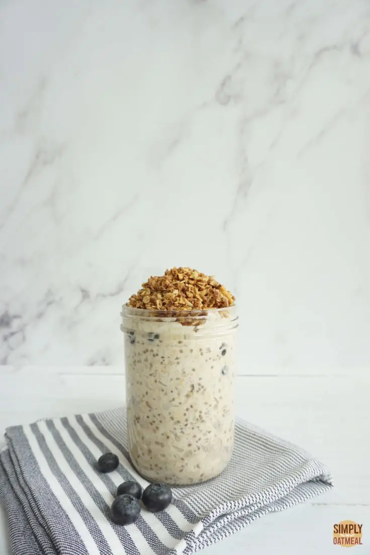 Glass jar filled with a serving of blueberry cobbler overnight oats. The jar is resting on top of a blue towel with fresh blueberries on the side.