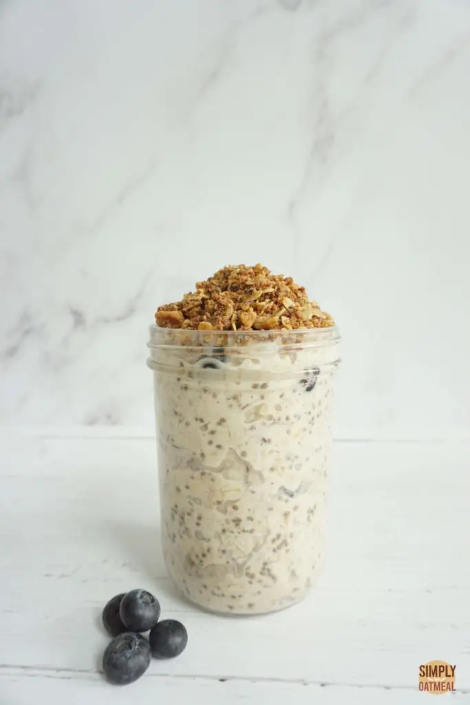 Tall mason jar with a single serving of blueberry cobbler overnight oats. The oatmeal is garnished with fresh blueberries and toasted cobbler topping.