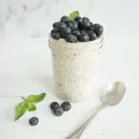 Single serving of blueberry muffin overnight oats in a mason jar. The oatmeal is topped with a pile of fresh blueberries and mint sprig