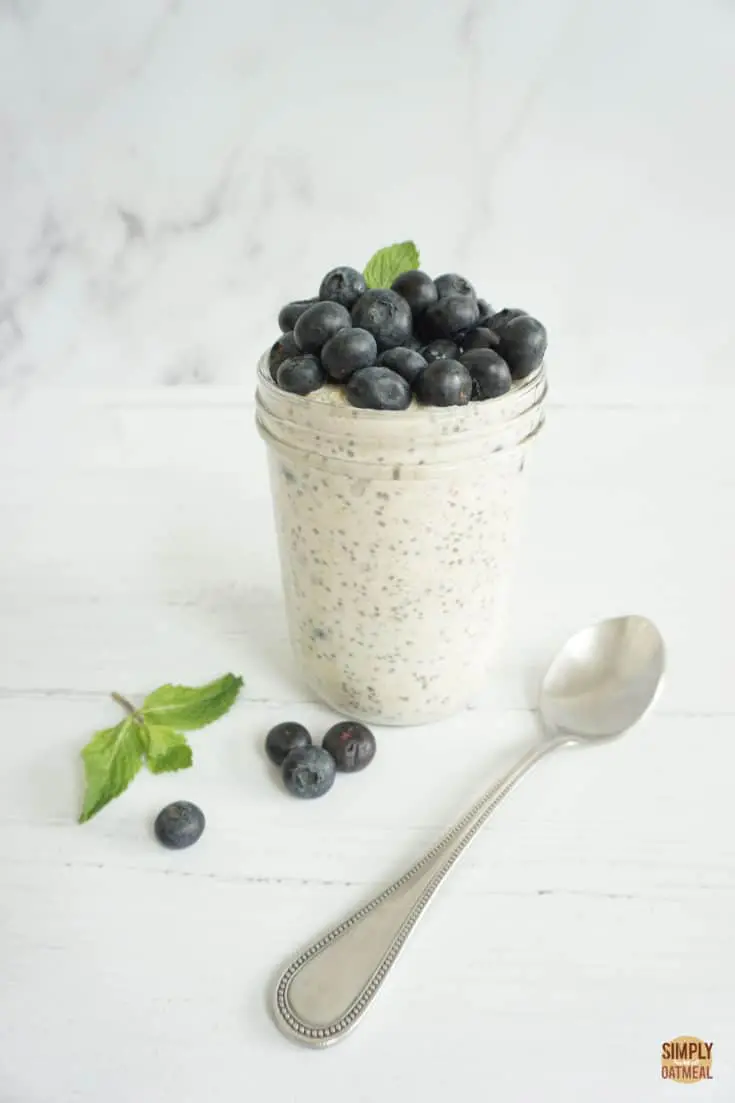 Single serving of blueberry muffin overnight oats in a mason jar. The oatmeal is topped with a pile of fresh blueberries and mint sprig