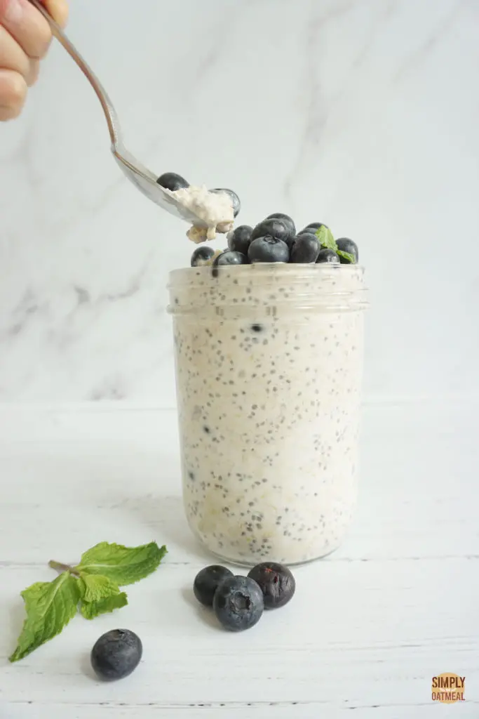 Spoon scooping a bite of blueberry muffin overnight oats from a glass jar.