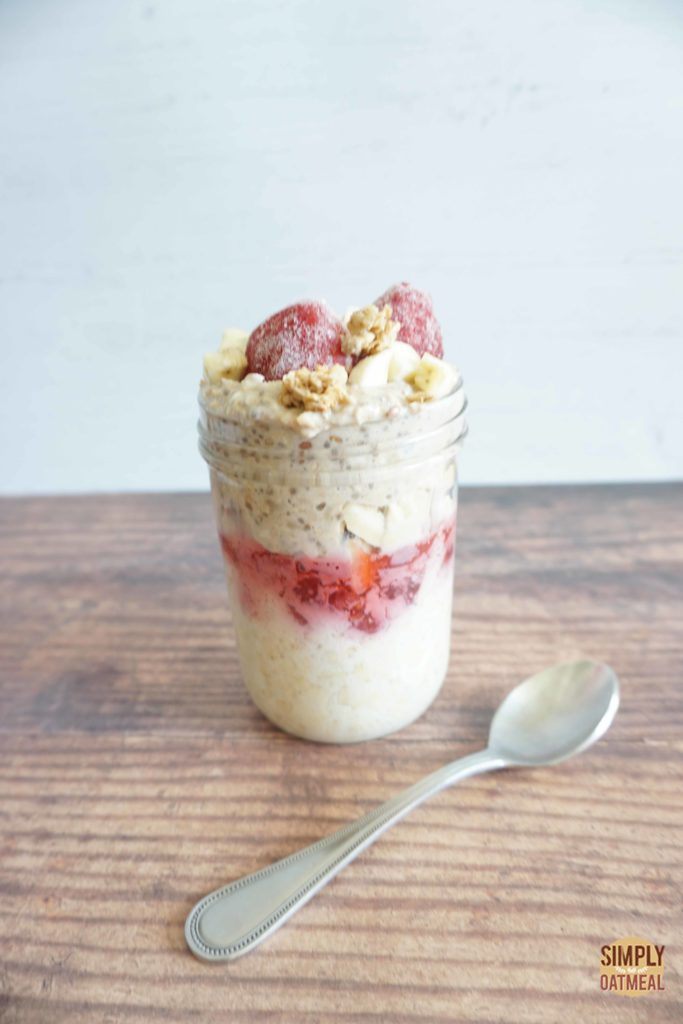 Strawberry banana overnight oats in a glass container with a spoon laying on the wood table