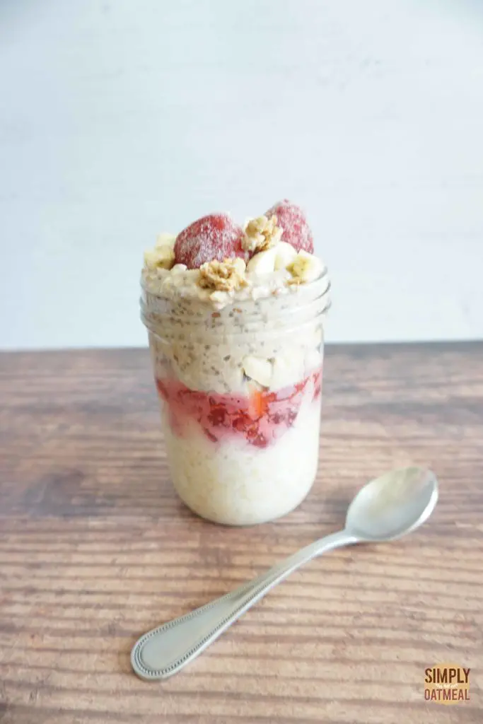 Strawberry banana overnight oats in a glass container with a spoon laying on the wood table