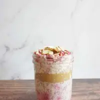 Single serving of raspberry almond overnight oats in a mason jar. A layer of almond butter is in the middle of the no cook oatmeal.