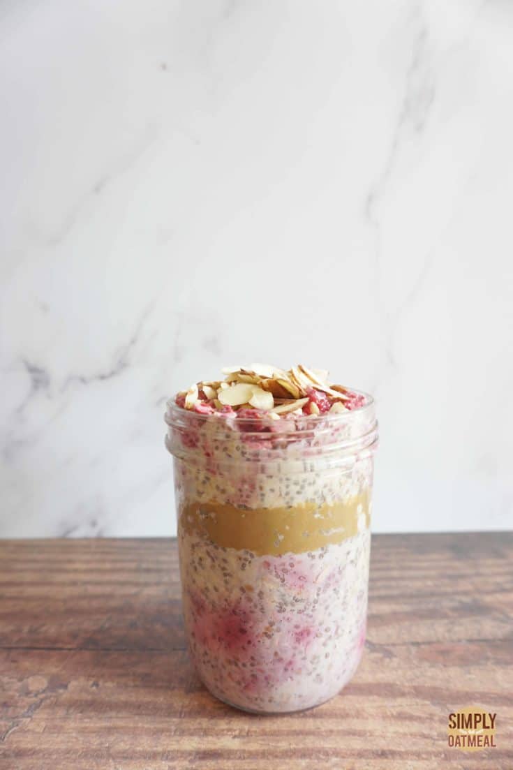Single serving of raspberry almond overnight oats in a mason jar. A layer of almond butter is in the middle of the no cook oatmeal.