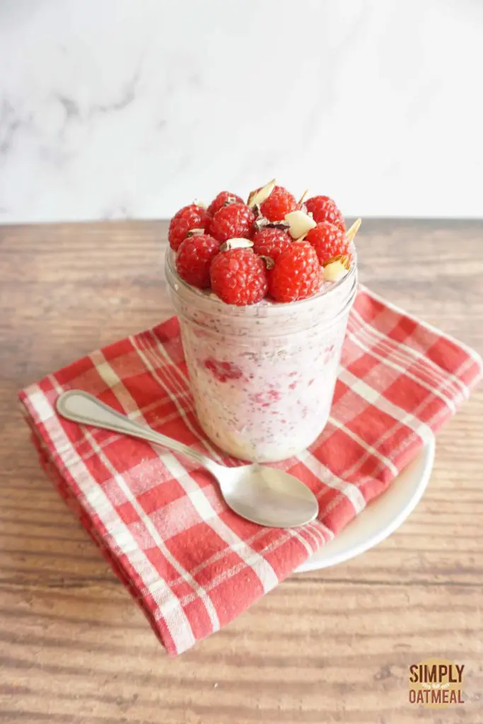 One serving of raspberry chia overnight oats in a mason jar with a spoon placed on the side.