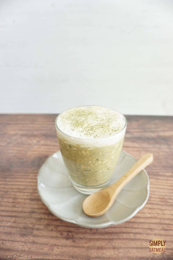 Single serving of green tea latte overnight oats in a glass cup with a wood spoon