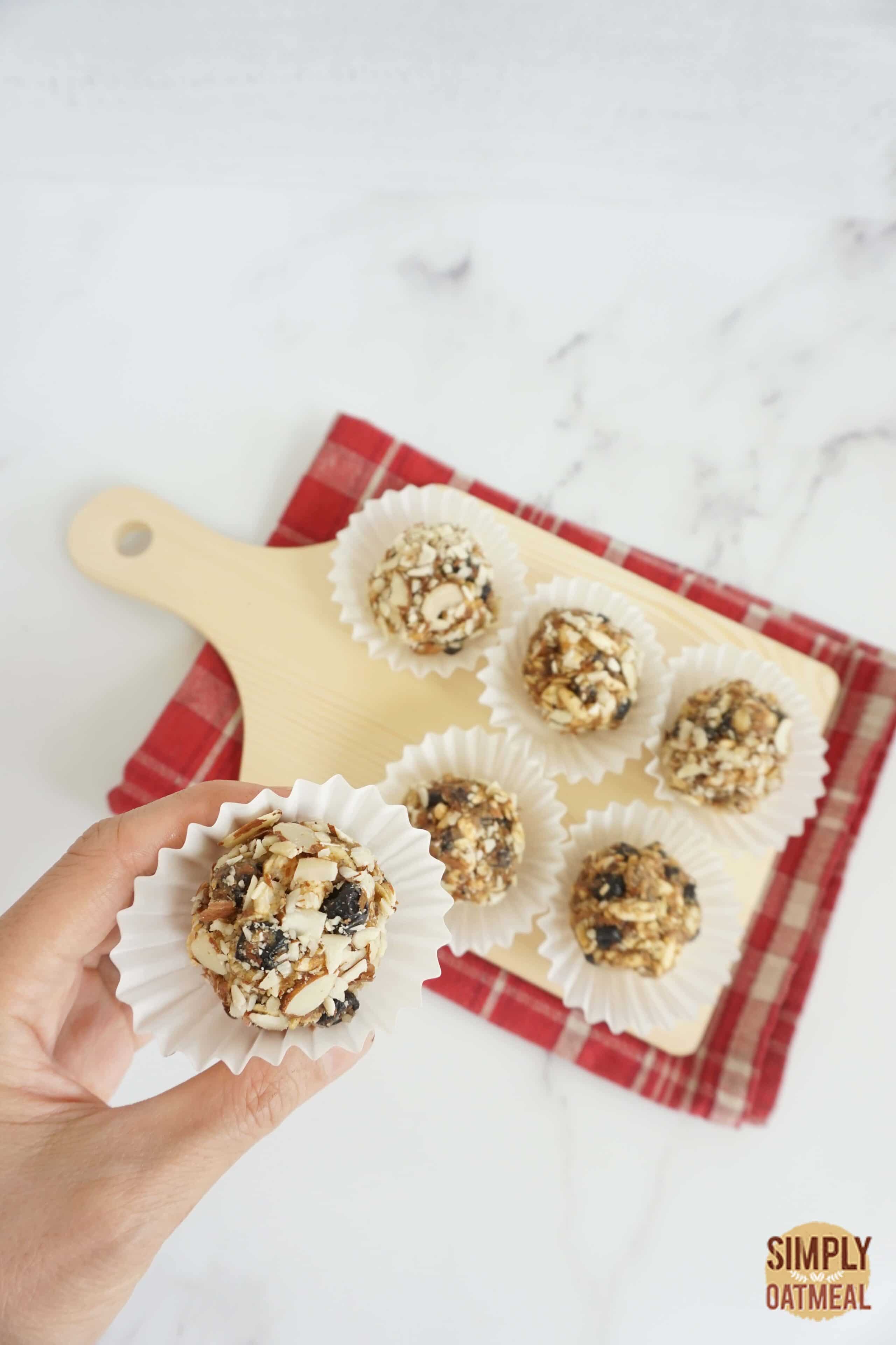 Hand holding one no bake blueberry muffin oatmeal ball in a paper liner