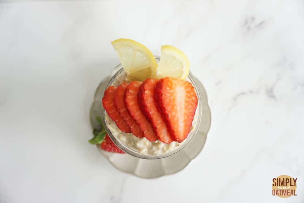 Lemon strawberry overnight oats served in a glass cup with fresh strawberries and sliced lemon
