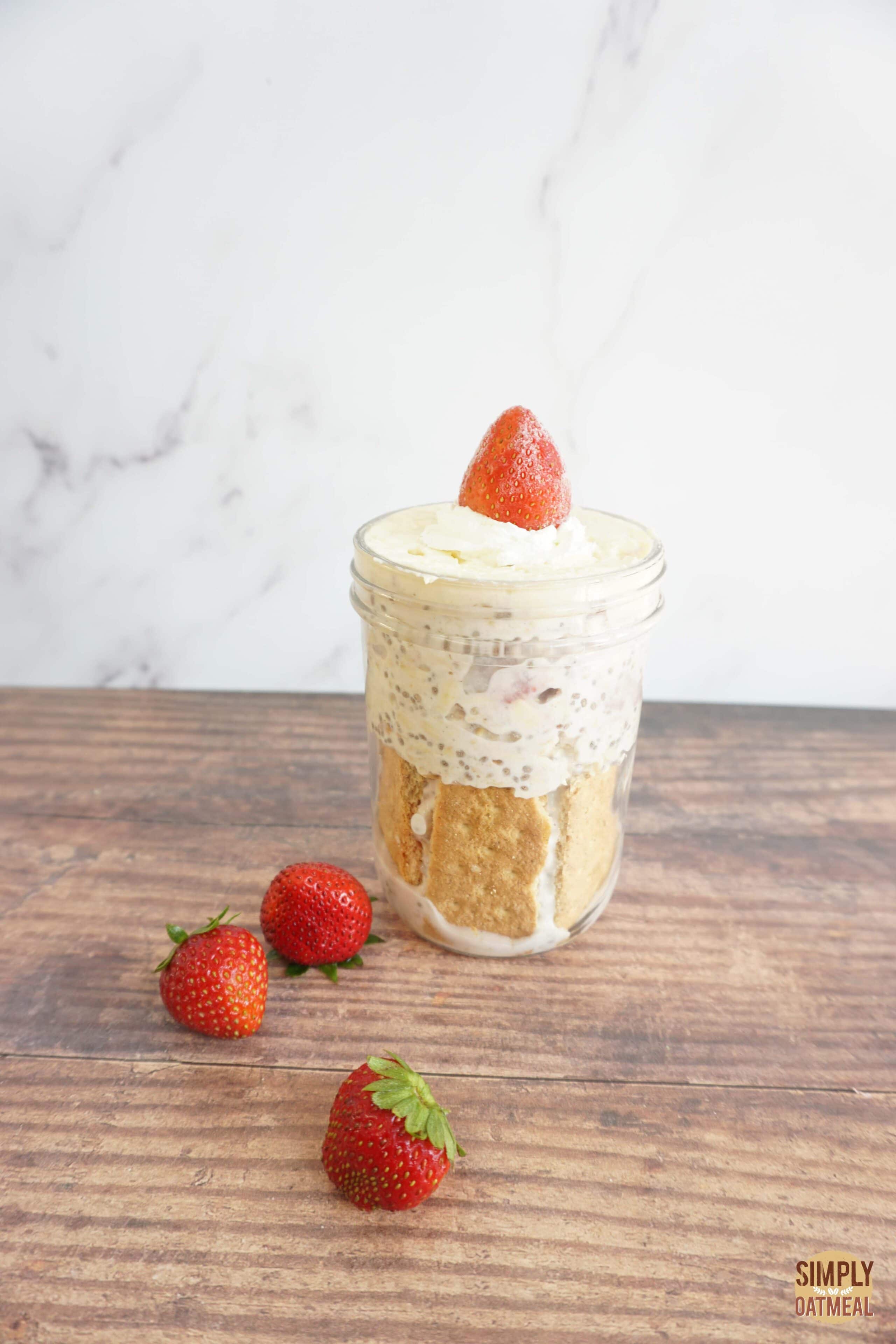 Strawberry cheesecake overnight oats served in a mason jar with graham cracker crust, cheese cake topping and sliced strawberries.