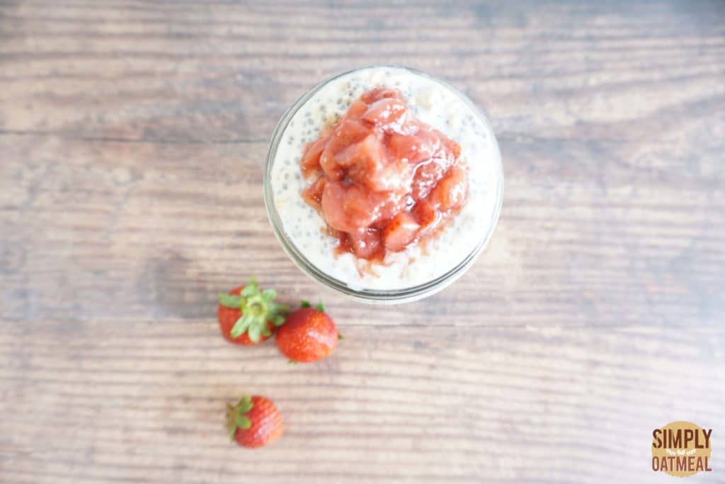 Serving of strawberry rhubarb overnight oats in a glass cup topped with strawberry and rhubarb on top