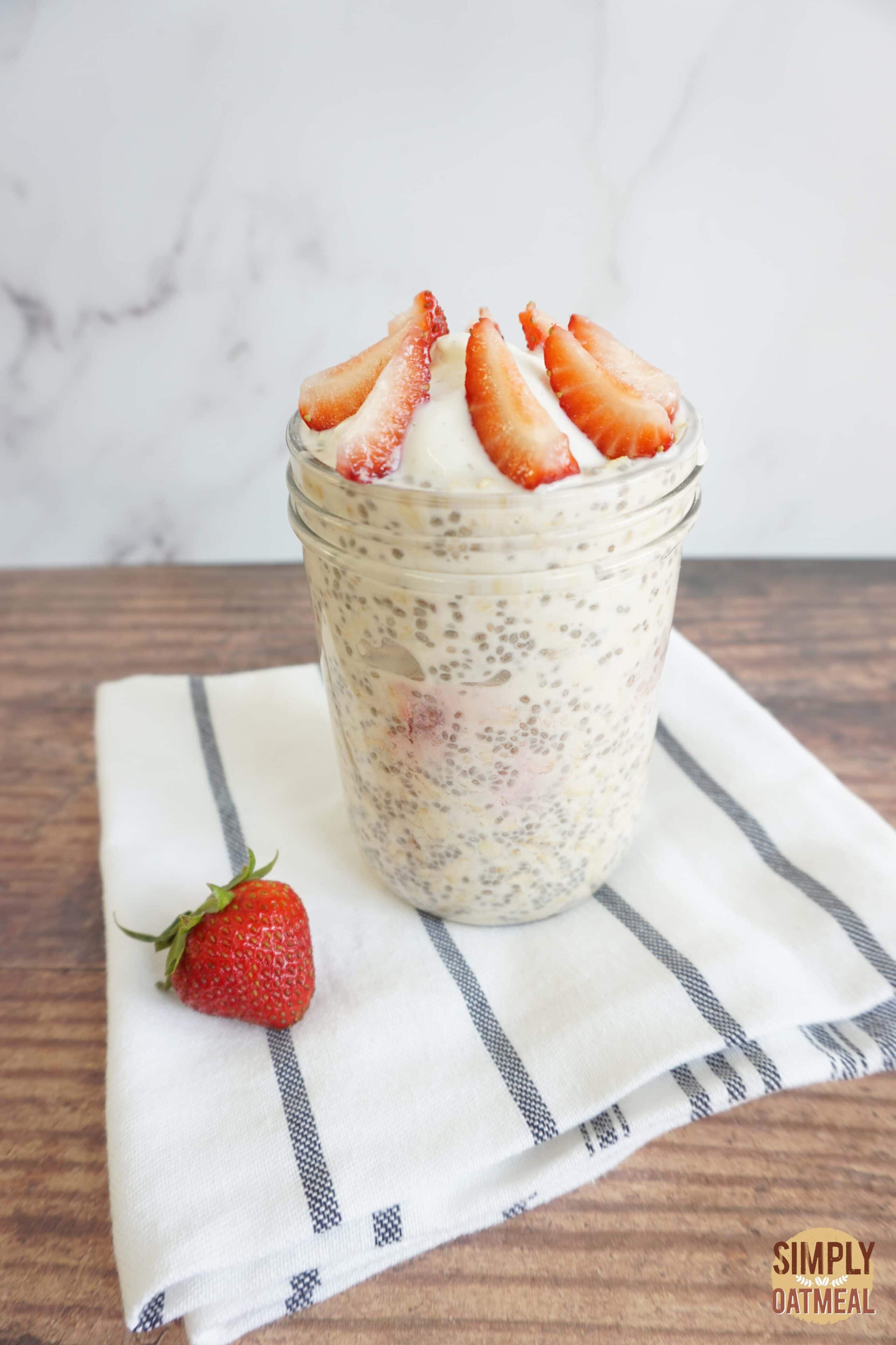 Strawberry vanilla overnight oats served in a mason jar garnished with vanilla whipped cream and fresh strawberries.