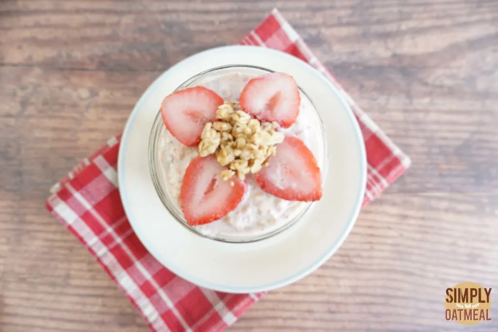 Serving of strawberry yogurt overnight oats in a glass cup garnished with sliced strawberry and crunchy granola